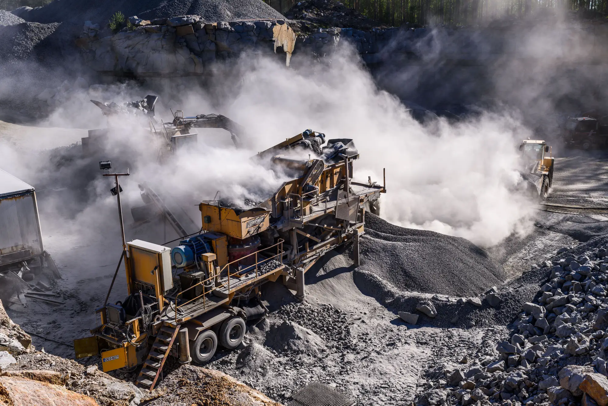 A mobile crusher at work in a rock quarry, a dust cloud rising off the feed and drifting across the pit floor
