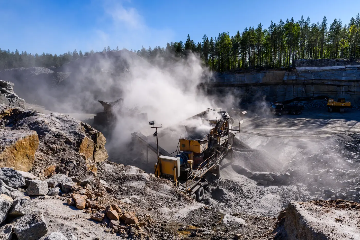 A dense white dust plume rises from rock-crushing equipment at a quarry, partly obscuring the machinery.